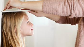 A girl being measured against the wall by her mother. 