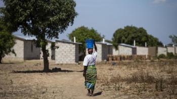 Margaret carries water from the nearby access point to her home built by Habitat Zambia, which feature concrete block construction and securely fastened roofs. 