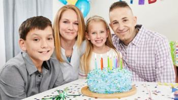 Mother, father, brother and sister celebrate son’s birthday with a cake and party at home.  