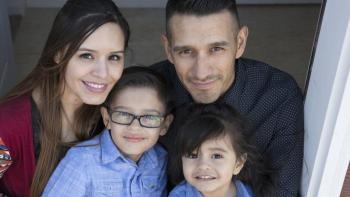 family of four smiling together in their doorway.