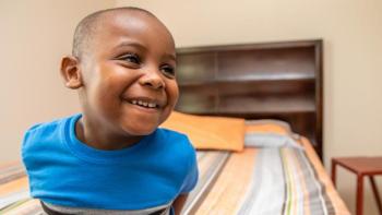 Boy smiling as he's sitting on his bed.