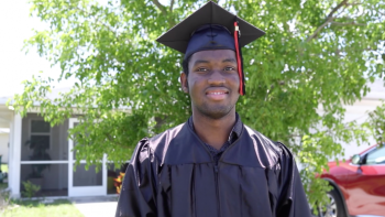 young man in graduation cap and gown smiling in front of his Habitat home.