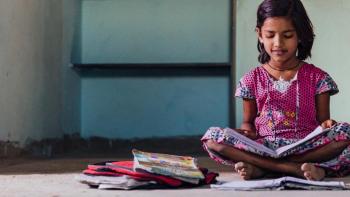 Young girl in India sits reading on her concrete floor.