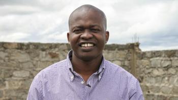 Kenyan man smiling in front of brick wall.