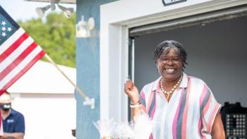 Lisa holding her key in front of her new home with an American flag hanging on the house.