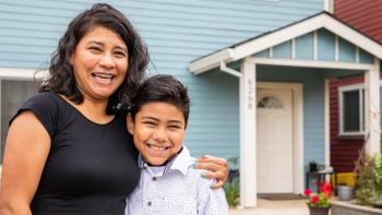 Mother and son smiling in front of blue house.