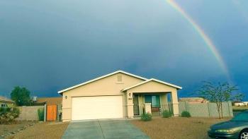 House with rainbow in the background against a dark sky.