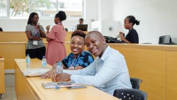 A pair of people sit together at a desk in a lecture hall.