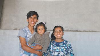 A mother and father stand together holding their baby.