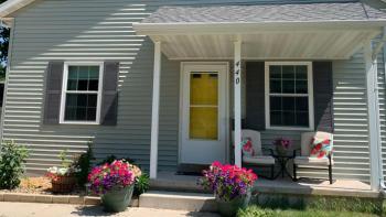 Habitat house with yellow door and pink flowers blooming in front.