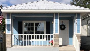 Photo: A blur house with a white roof and a front gated patio.
