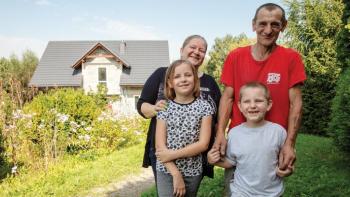 Family of four smiling together in the flower garden in front of their home.