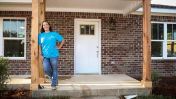 Woman in blue shirt standing on the front stoop of her home.