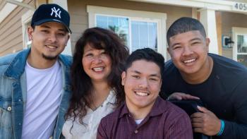 Woman and three young adult sons smiling together in front of their home.
