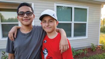 Two adolescent brothers smiling together in the yard in front of their home.