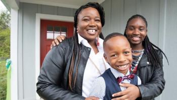 Woman with daughter and young son smiling in front of their home.