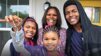 Mother smiling with three children and youngest daughter is holding up their house key.