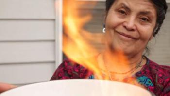 Maria holding up a bowl that contains a fire burning her mortgage papers.