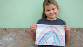 little girl holding up drawing of a rainbow.