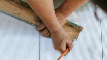 A worker measuring wood with a ruler and pencil.