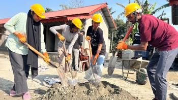 Four young people in yellow hardhats with shovels working on a project.