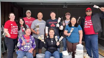 A group of State Farm employees posing with paint and paint brushes in front of a garage.