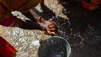 View from above of a woman in an orange sari washing her hands over a bucket of sudsy water.