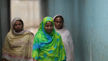 A woman in vibrant green clothing leads two other women down an alleyway in an informal community.