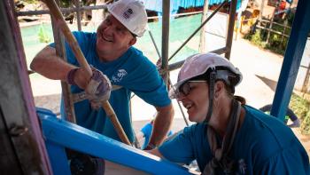 Two volunteers on a build site in white hard hats. 