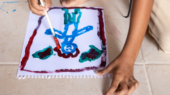 A painted figure in blue and red with a little kids hands and knees appearing in the frame as they paint.