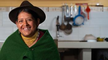 A woman shown from the waist up in her home kitchen.
