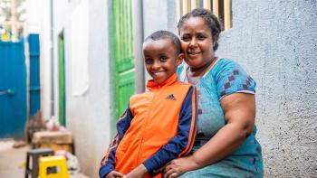 A woman and her son sit outside their home smiling