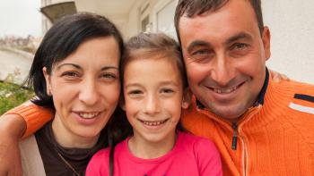 A mother, father and young daughter smiling together outside.