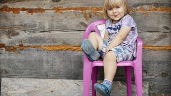 small child sitting in child-sized pink plastic chair in front of rustic wood wall
