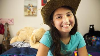 Smiling girl in cowboy hat sitting in bedroom