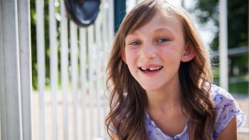 A little girl smiling and sitting outside her home.