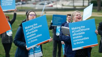 Two advocates in a crowd of several with blue signs that read "Cost of Home" outside the White House.