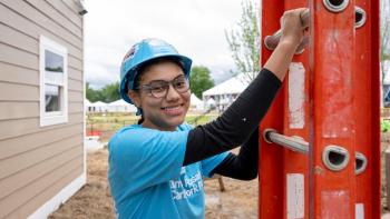 A volunteer smiles for a photo while holding a ladder at a work site. 
