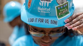 Woman tilting her head forward to show the stickers on her blue Habitat hard hat. The stickers say, "A-Town Down," "Welcome to Atlanta," and "I did it for us, son!"