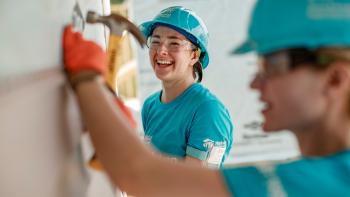 Two women smiling on the build site, one is hammering.