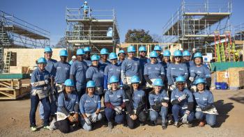 Group of US Bank employees posing in blue shirts and bright blue hard hats on a job site.