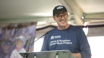 Jonathan Reckford smiling at a podium, wearing a Carter Work Project shirt.