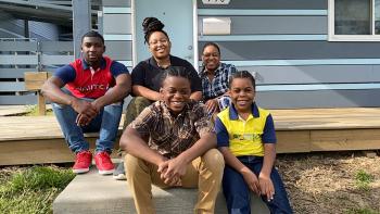 Star and her family of five sitting in front of their blue Habitat home.