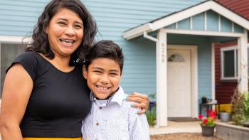 A mother and her son stand outside a blue home.