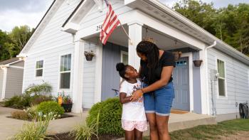 Mother and daughter smiling at each other while standing in front of house