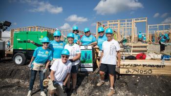 A group of Bank of America employees pose in bright blue hard hats on a job site.