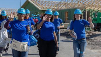 Volunteers in dark blue Ford shirts and light blue Habitat hard hats wave as they arrive on a build site.