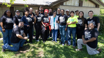 A group of volunteers wearing yellow Habitat shirts and black Hotties Helping shirts pose with a homeowner.