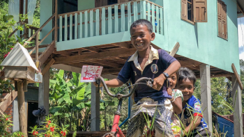 Cambodian children riding bikes in front of their home.