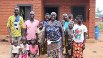 Large group smiling in front of brick home in Côte d’Ivoire.